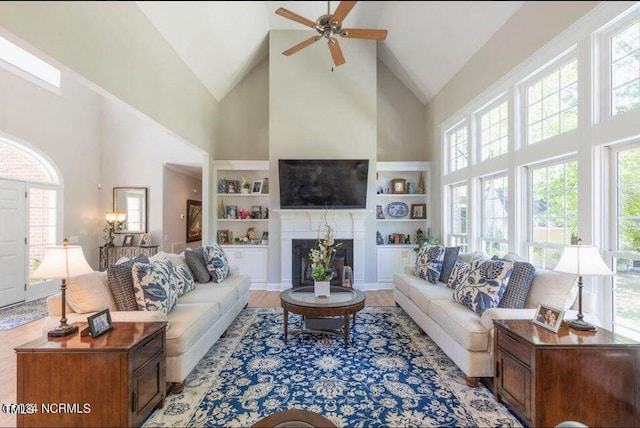 living area featuring high vaulted ceiling, a ceiling fan, plenty of natural light, built in features, and a fireplace