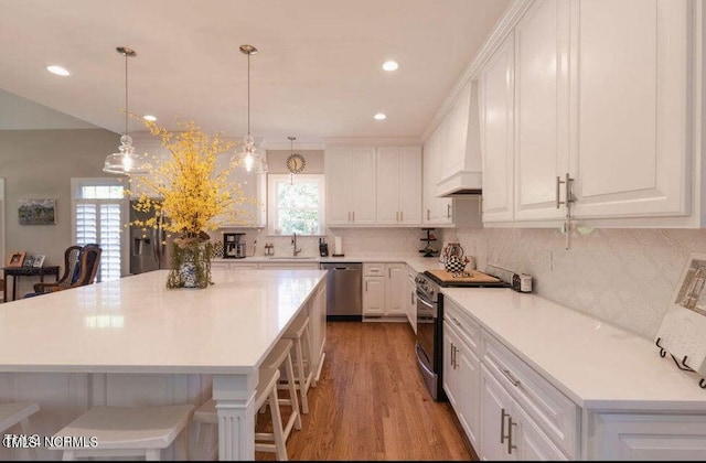 kitchen featuring a kitchen breakfast bar, stainless steel appliances, white cabinetry, light wood-type flooring, and premium range hood