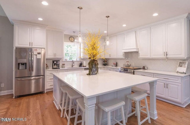 kitchen with appliances with stainless steel finishes, premium range hood, white cabinetry, light hardwood / wood-style floors, and sink