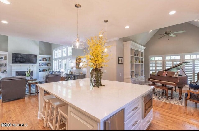 kitchen with open floor plan, stainless steel microwave, light wood finished floors, recessed lighting, and high vaulted ceiling