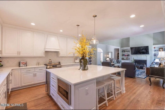 kitchen with white cabinets, custom range hood, stainless steel appliances, and light hardwood / wood-style floors