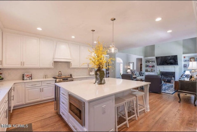 kitchen with stainless steel microwave, premium range hood, white cabinetry, a kitchen island, and a fireplace
