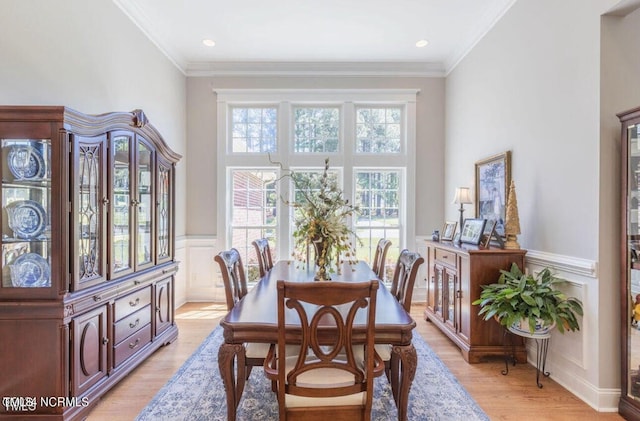 dining space featuring light wood-type flooring, wainscoting, a decorative wall, and ornamental molding