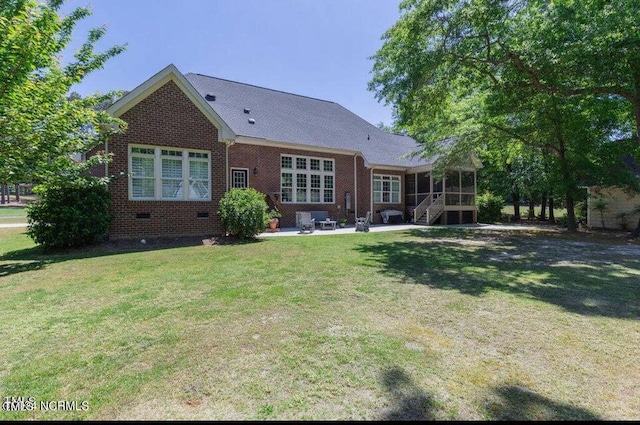 rear view of house with a sunroom, brick siding, a patio, a lawn, and crawl space