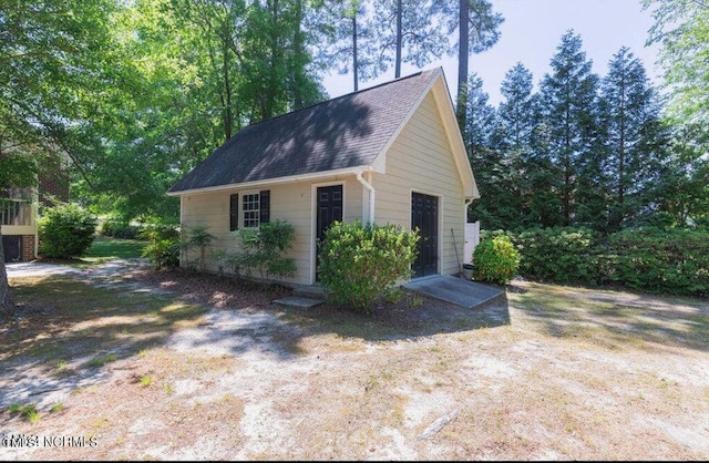 view of side of home with a shingled roof and an outbuilding