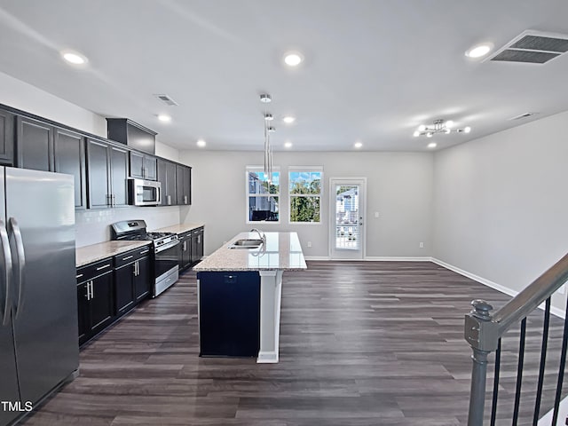 kitchen with an island with sink, stainless steel appliances, sink, pendant lighting, and light stone counters