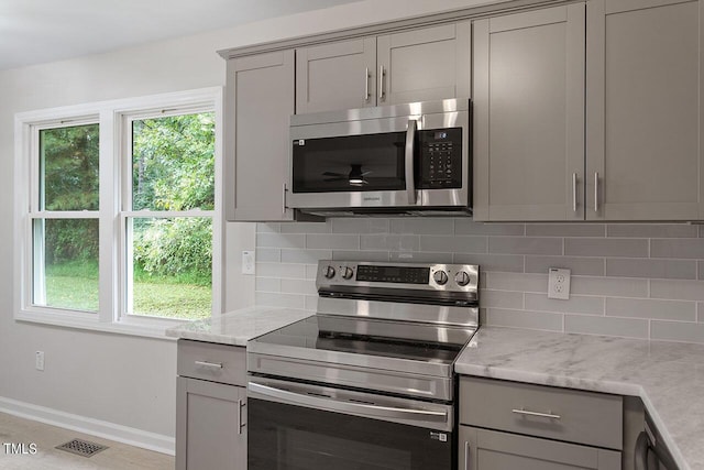 kitchen featuring appliances with stainless steel finishes, light stone counters, backsplash, and gray cabinets