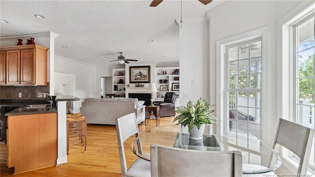 dining room featuring sink, a textured ceiling, ceiling fan, ornamental molding, and light hardwood / wood-style flooring