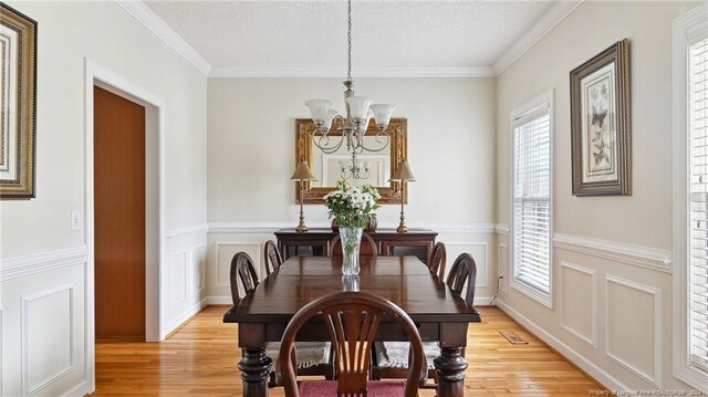 dining room featuring crown molding, a textured ceiling, an inviting chandelier, and light wood-type flooring