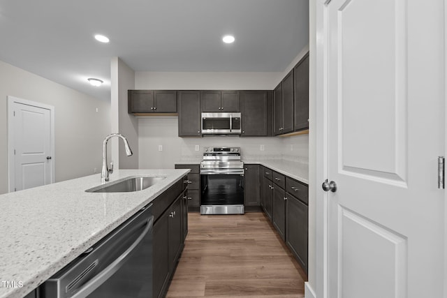 kitchen with sink, light stone counters, wood-type flooring, dark brown cabinets, and appliances with stainless steel finishes