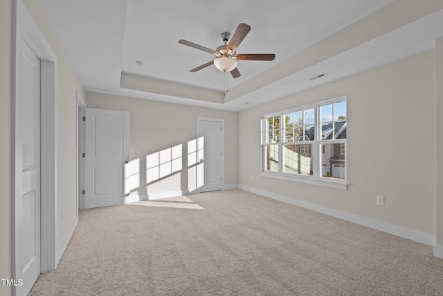 carpeted spare room with a raised ceiling and ceiling fan