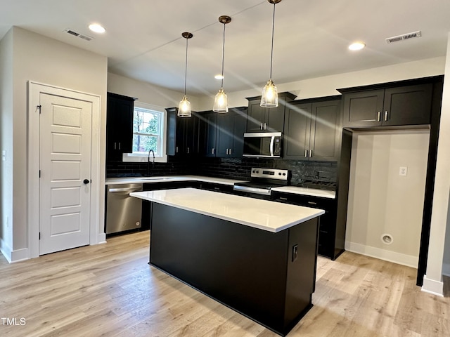 kitchen with a center island, hanging light fixtures, light wood-type flooring, and appliances with stainless steel finishes