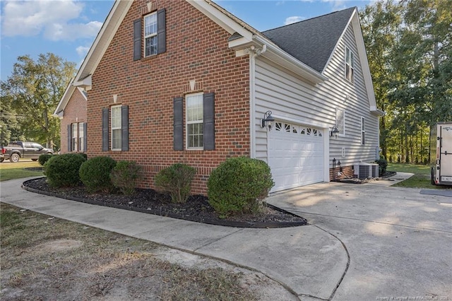 view of side of home with a garage, a shingled roof, central AC unit, concrete driveway, and brick siding