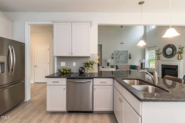 kitchen featuring stainless steel appliances, white cabinets, sink, light wood-type flooring, and decorative light fixtures