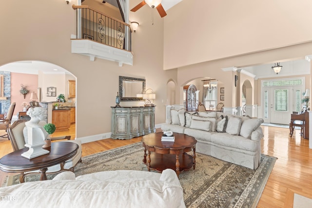 living room with a towering ceiling, light hardwood / wood-style flooring, ceiling fan with notable chandelier, and ornamental molding