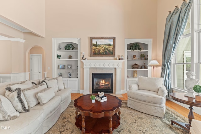 living room featuring light hardwood / wood-style floors, a towering ceiling, a healthy amount of sunlight, and built in shelves