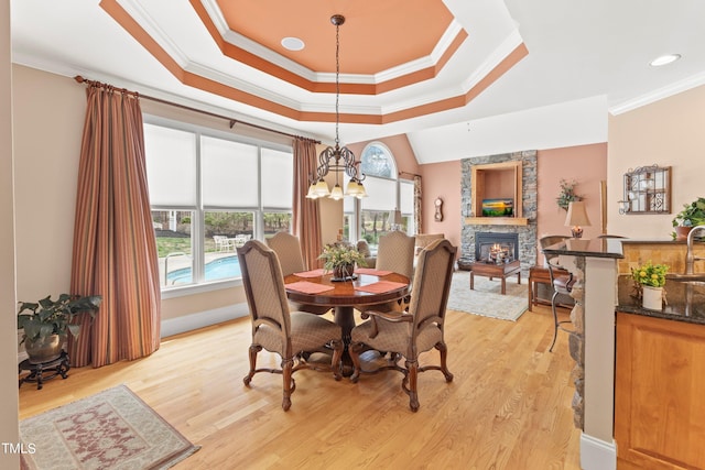 dining area with a fireplace, a tray ceiling, crown molding, a notable chandelier, and light hardwood / wood-style flooring