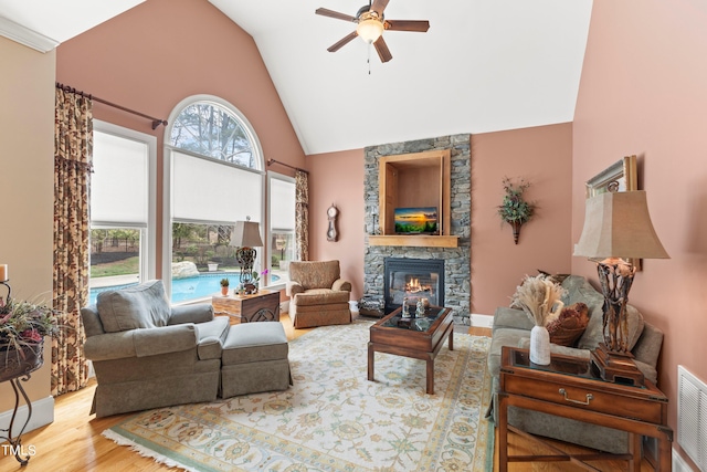 living room with a stone fireplace, hardwood / wood-style floors, high vaulted ceiling, and ceiling fan