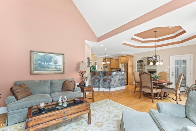 living room featuring a chandelier, light hardwood / wood-style flooring, crown molding, and a raised ceiling