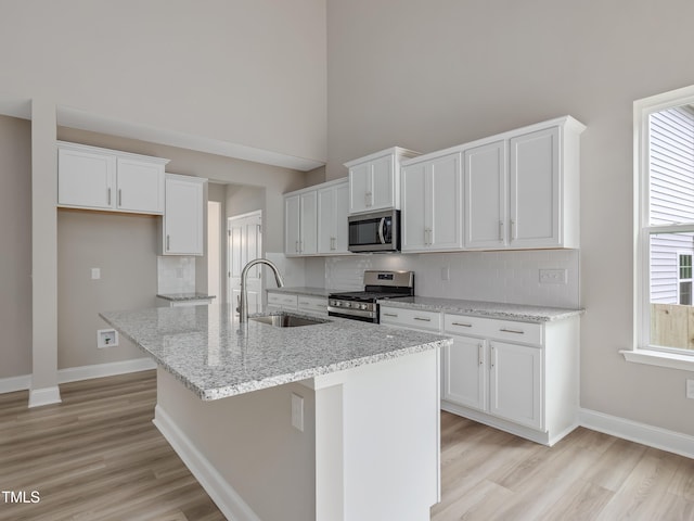 kitchen with appliances with stainless steel finishes, a kitchen island with sink, sink, light hardwood / wood-style flooring, and white cabinets