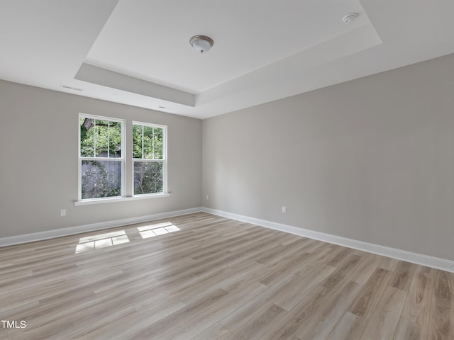 spare room featuring a tray ceiling and light hardwood / wood-style floors