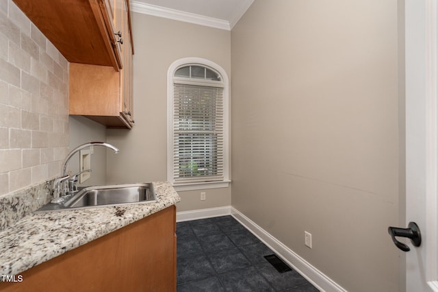 kitchen with light stone countertops, dark tile patterned flooring, ornamental molding, and sink