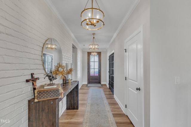 foyer with brick wall, light wood-type flooring, crown molding, and an inviting chandelier