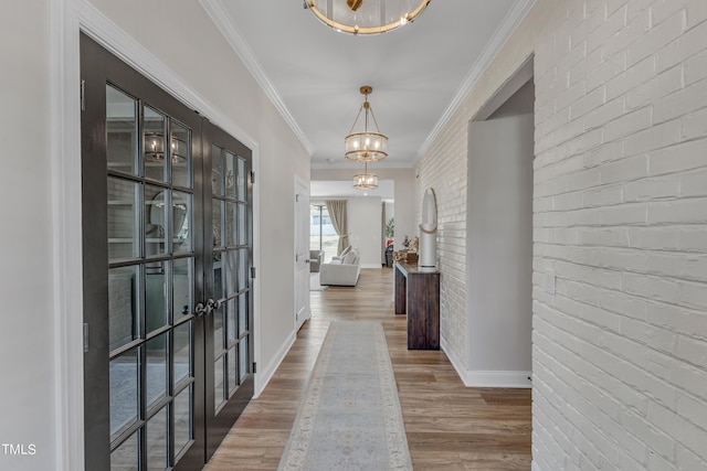 hallway with brick wall, wood-type flooring, french doors, ornamental molding, and a notable chandelier