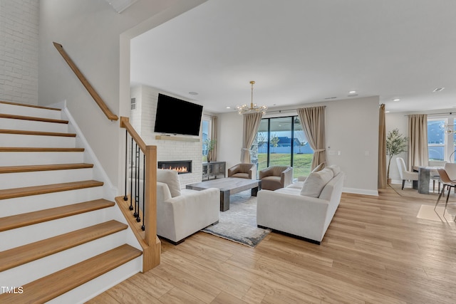 living room featuring stairs, a chandelier, light wood-style floors, a brick fireplace, and baseboards