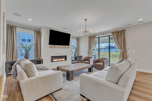 living room featuring light wood-type flooring, a brick fireplace, and an inviting chandelier