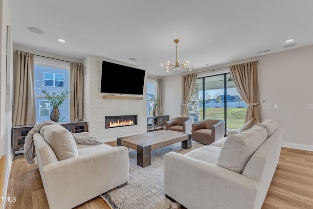 living area featuring wood finished floors, baseboards, a notable chandelier, and a brick fireplace