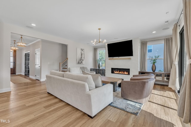 living room featuring a large fireplace, light hardwood / wood-style flooring, ornamental molding, and a notable chandelier