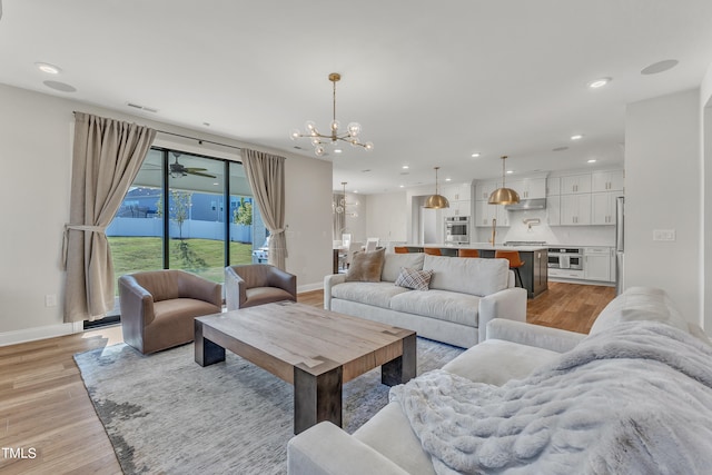 living room featuring light wood-type flooring and ceiling fan with notable chandelier