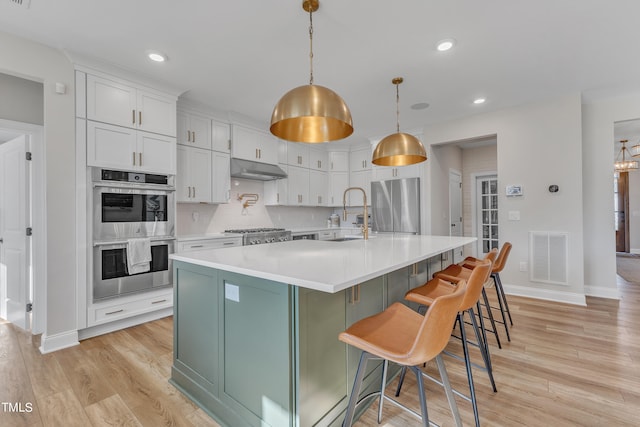 kitchen featuring white cabinetry, stainless steel appliances, decorative light fixtures, a kitchen breakfast bar, and sink