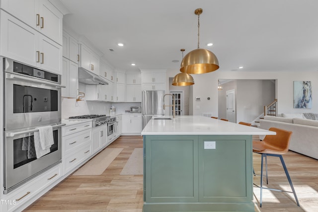 kitchen featuring a center island with sink, appliances with stainless steel finishes, white cabinets, and a breakfast bar area