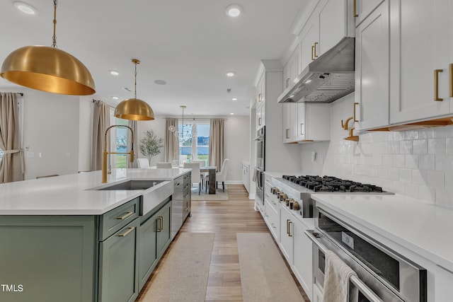 kitchen featuring ventilation hood, decorative backsplash, decorative light fixtures, a kitchen island with sink, and sink