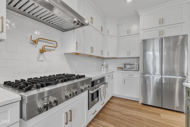 kitchen with range hood, light hardwood / wood-style floors, decorative backsplash, white cabinetry, and stainless steel appliances