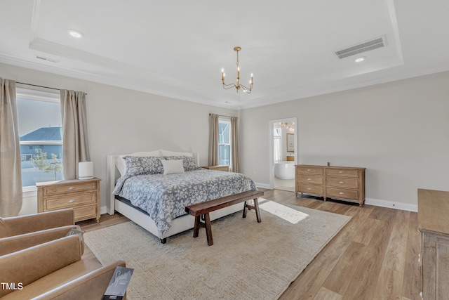 bedroom featuring an inviting chandelier, ensuite bathroom, light hardwood / wood-style floors, and a tray ceiling