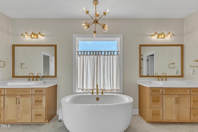 bathroom featuring an inviting chandelier, two vanities, a freestanding tub, and a sink