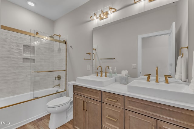 full bathroom with combined bath / shower with glass door, vanity, wood-type flooring, and toilet