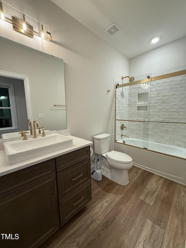 full bathroom with wood-type flooring, enclosed tub / shower combo, vanity, and toilet