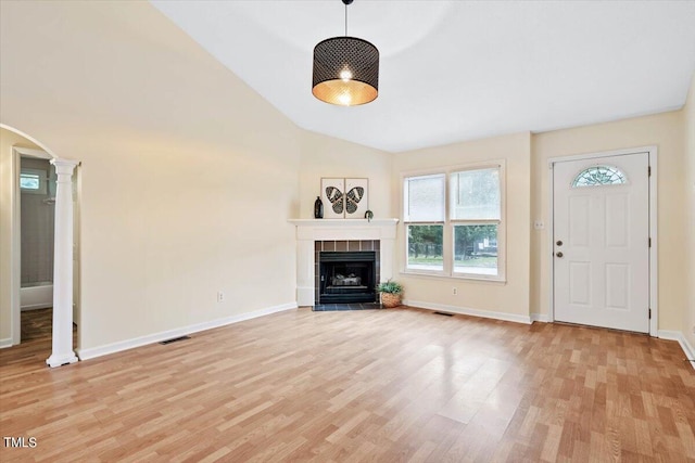 unfurnished living room with lofted ceiling, light hardwood / wood-style flooring, ornate columns, and a tile fireplace