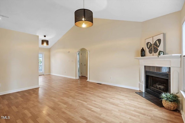 unfurnished living room featuring a tiled fireplace, light hardwood / wood-style floors, and high vaulted ceiling