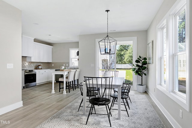 dining space featuring a notable chandelier, a healthy amount of sunlight, sink, and light wood-type flooring