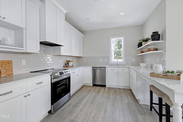 kitchen with tasteful backsplash, sink, white cabinetry, light hardwood / wood-style floors, and stainless steel appliances