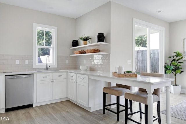 kitchen featuring backsplash, white cabinetry, dishwasher, light hardwood / wood-style floors, and sink