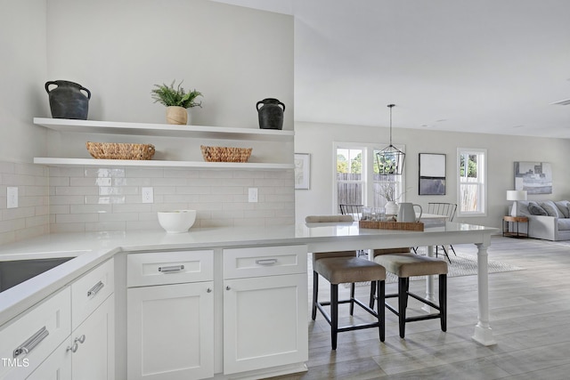 kitchen with tasteful backsplash, white cabinetry, a kitchen bar, pendant lighting, and light hardwood / wood-style floors