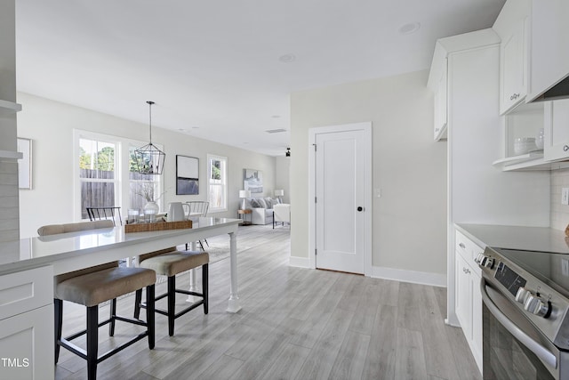 kitchen with white cabinets, stainless steel range with electric cooktop, hanging light fixtures, a chandelier, and light hardwood / wood-style flooring