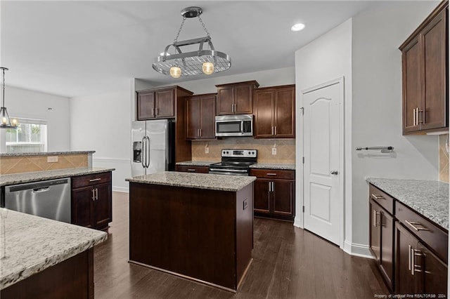 kitchen with dark hardwood / wood-style floors, stainless steel appliances, a center island, decorative light fixtures, and light stone counters