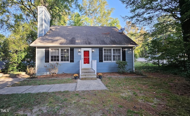 view of front of property with a shingled roof, a chimney, and a front yard